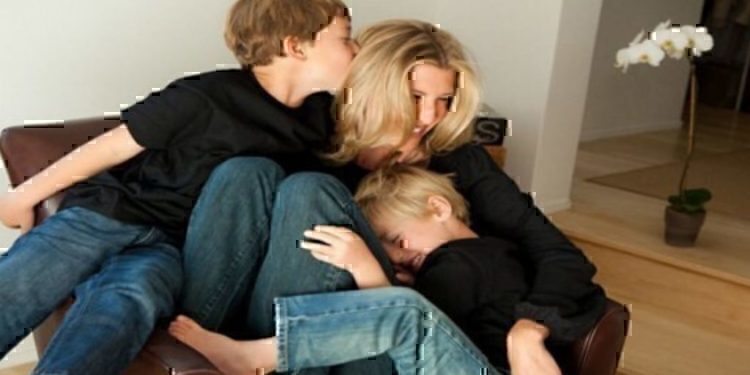 A mother sitting on a chair while playing with her two young boys.