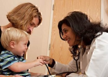 A doctor leaning down to smile and play with a young child.