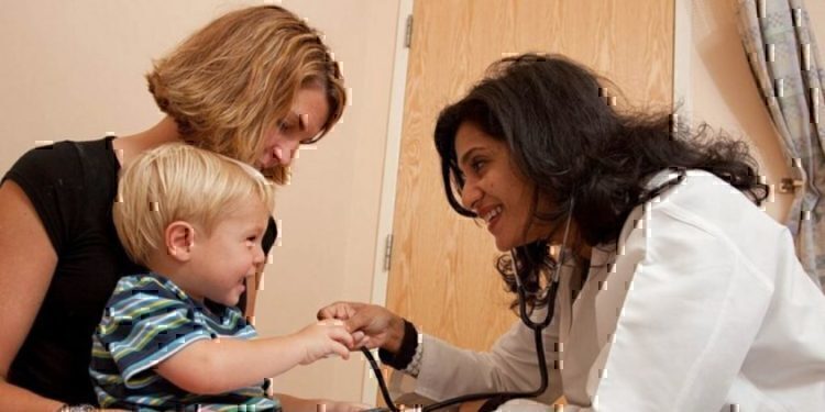 A doctor leaning down to smile and play with a young child.