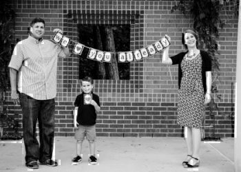 A mother and a father holding up a sign in front of their home.