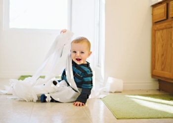 A young child getting wrapped up in toilet paper.