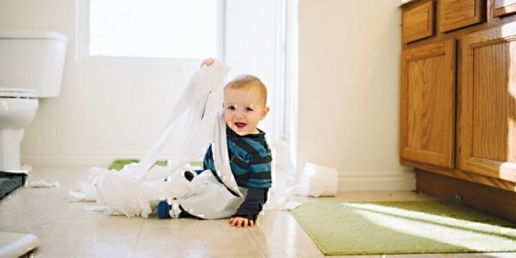 A young child getting wrapped up in toilet paper.