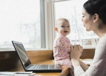 A mother working on her laptop while entertaining her young child.