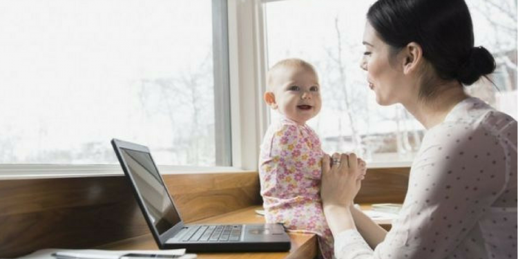 A mother working on her laptop while entertaining her young child.