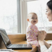 A mother working on her laptop while entertaining her young child.