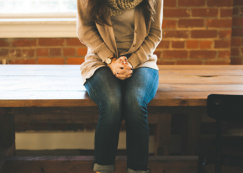 A young women sitting on a table with her hands folded.