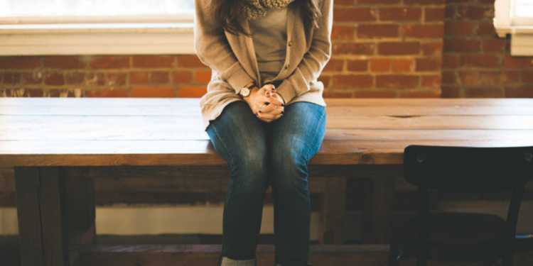 A young women sitting on a table with her hands folded.