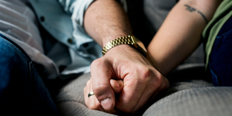 A couple holding hands while sitting on a couch.