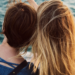 Two women sitting down and leaning on each other while they look out over the water.