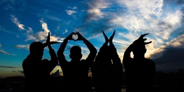 Four people sitting down spelling out the word love with their hands.