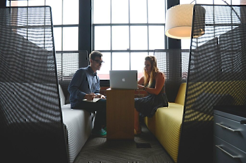 A man and a women seated down looking at a computer to discuss a business idea.