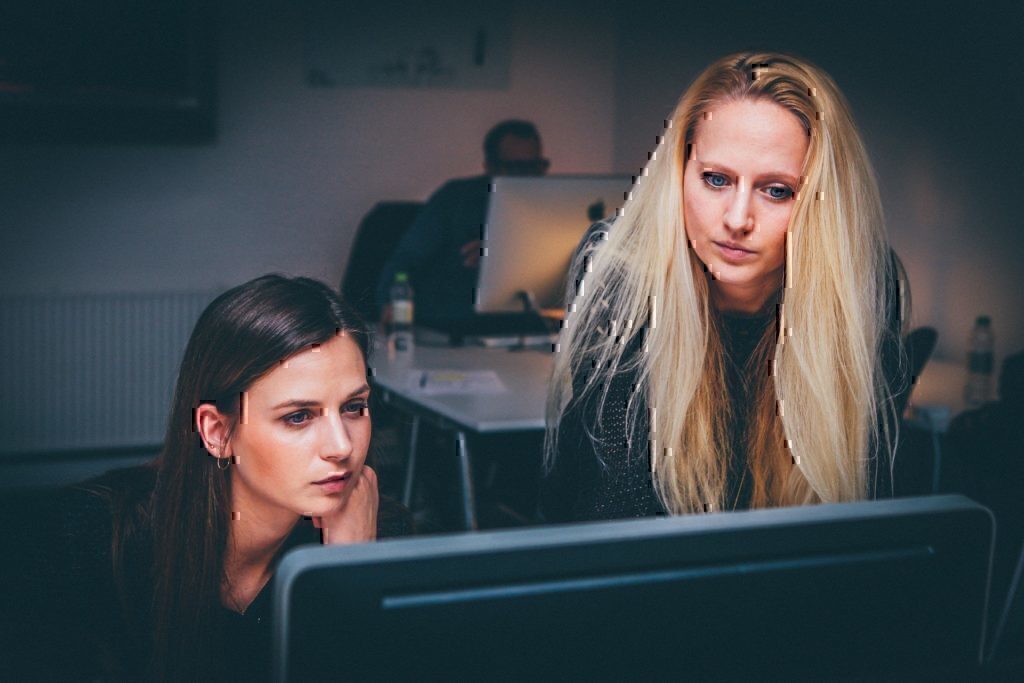 Two women leaning over a computer during their work day.