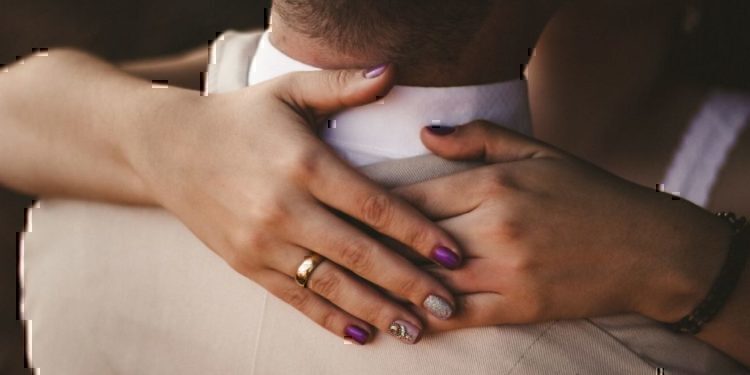 A wife wrapping her hands around her husbands neck.