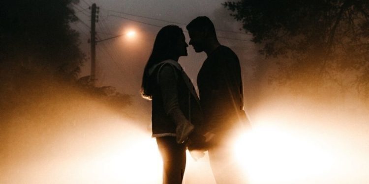 A young couple holding hands while looking into each others eyes.