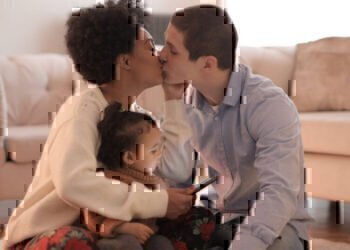 A service member and his wife kissing while holding their child.