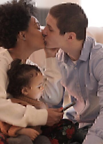 A service member and his wife kissing while holding their child.