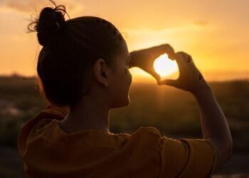 A women making a heart with her hands, and holding it up to the sun.