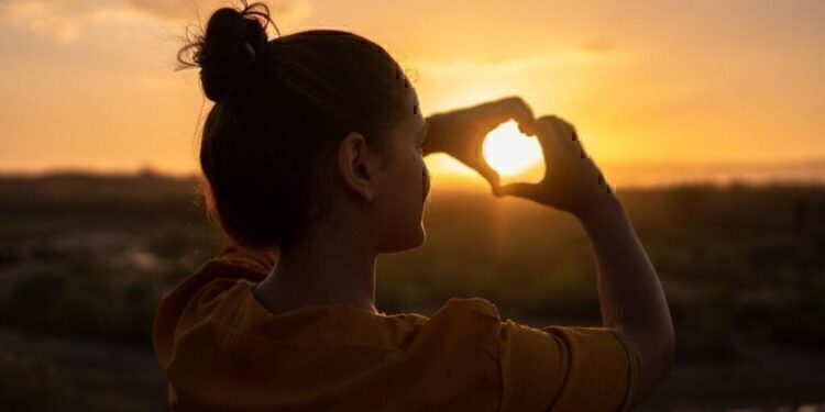 A women making a heart with her hands, and holding it up to the sun.