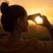 A women making a heart with her hands, and holding it up to the sun.