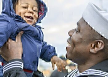 A Navy seamen lovingly picks up his smiling baby boy after coming home from deployment