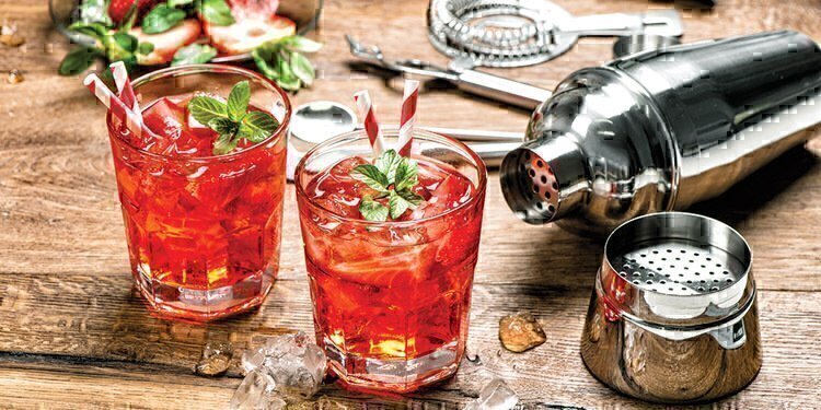 Two strawberry cocktails at the fore-front with the ingredients and shaker in the background.