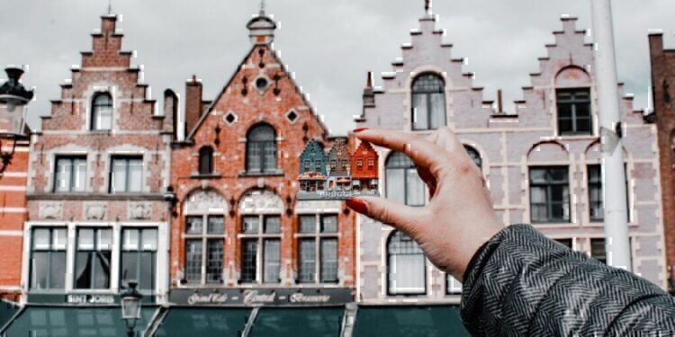 Someone's hand holding up a set of little homes, compared to bigger homes.