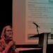 A women sitting down at a conference, talking about mental health.