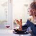 A women looking out of her window while eating her lunch alone.