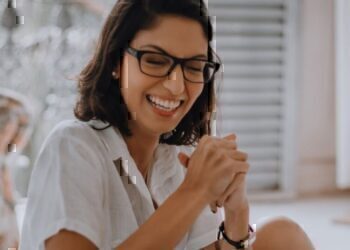 A women sitting down, while smiling and holding her hands together.