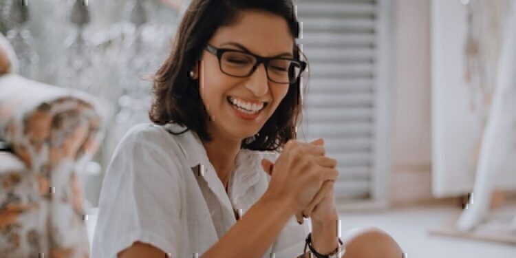 A women sitting down, while smiling and holding her hands together.