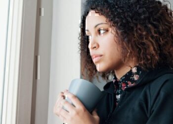 A women looking thoughtfully out of her window while holding a cup of coffee.