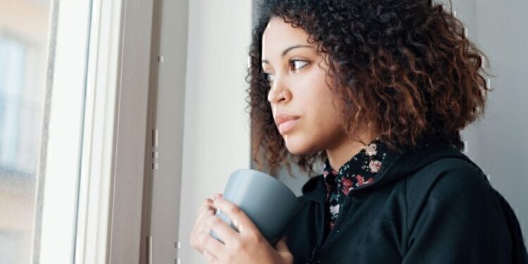 A women looking thoughtfully out of her window while holding a cup of coffee.