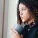 A women looking thoughtfully out of her window while holding a cup of coffee.