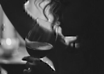 A black and white photo of a women holding up a wine glass, about to take another drink.