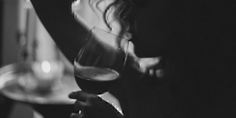 A black and white photo of a women holding up a wine glass, about to take another drink.