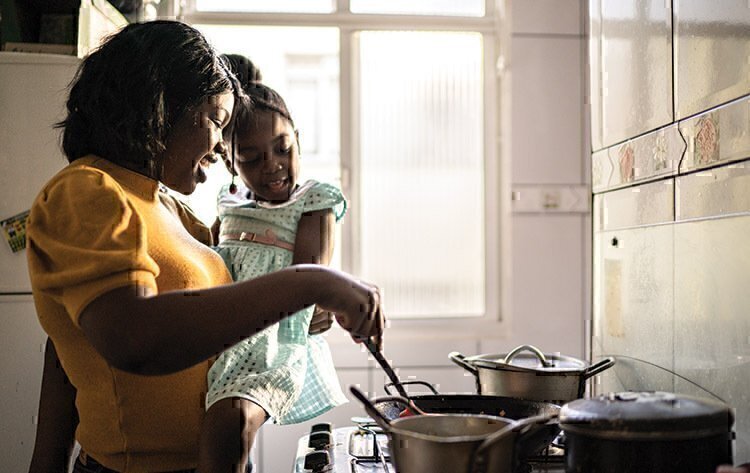 A mother holding her daughter while stirring dinner together.