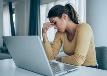 Stressed woman working from home. Frustrated businesswoman with head in hands sitting on the desk at home. Overworked young businesswoman sitting in front of laptop and holding head. Home office concept.