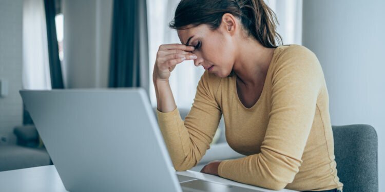 Stressed woman working from home. Frustrated businesswoman with head in hands sitting on the desk at home. Overworked young businesswoman sitting in front of laptop and holding head. Home office concept.