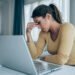 Stressed woman working from home. Frustrated businesswoman with head in hands sitting on the desk at home. Overworked young businesswoman sitting in front of laptop and holding head. Home office concept.